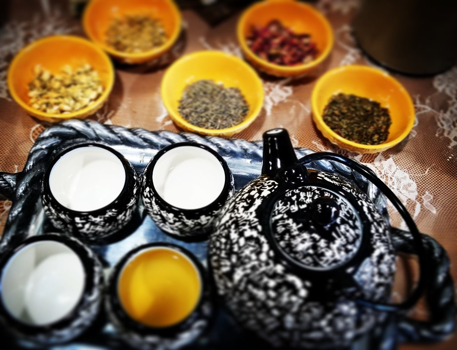 A black teapot, cups, and bowls of herbs arranged for a Blu Lady Wellness tea ritual